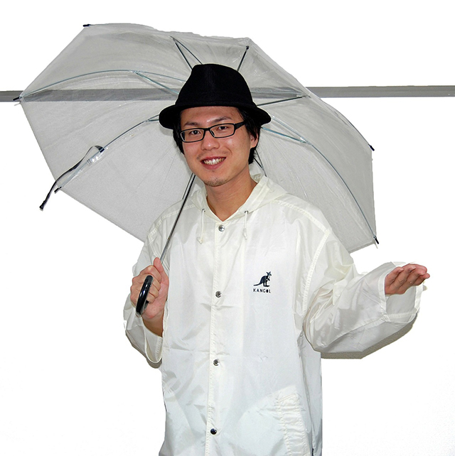 傘を差し、レインコートを着て微笑む男性